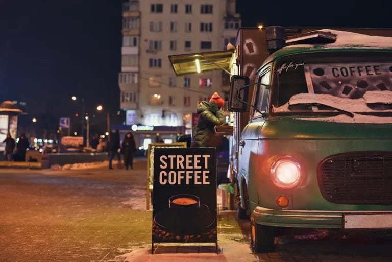 A person orders from a green coffee food truck on a snowy night.