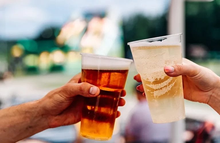 Two people clinking plastic cups full of beer outdoors.