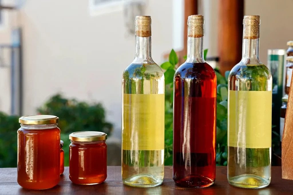 Bottles of wine and jars of honey on a countertop at an outdoor market.