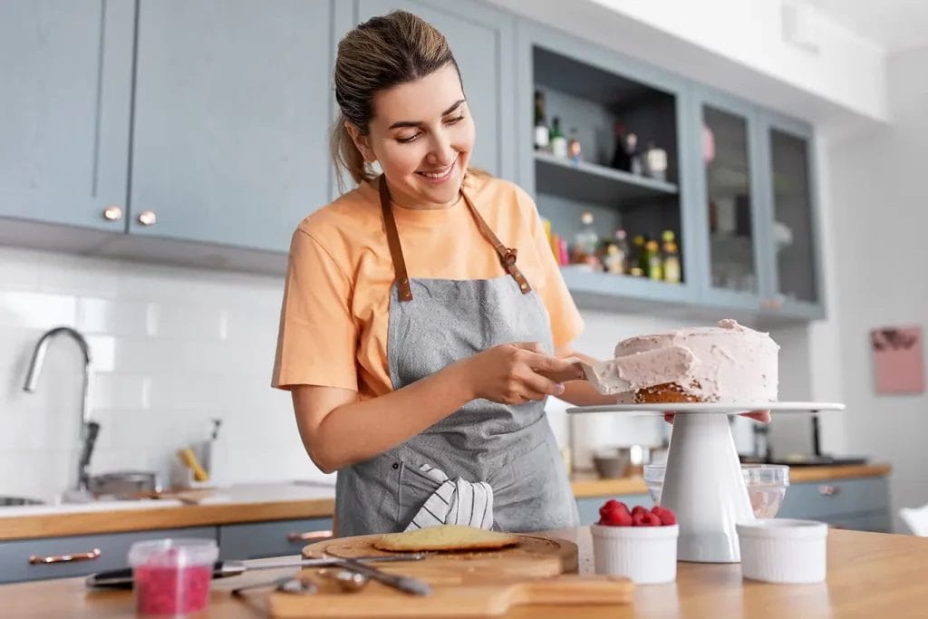 Woman standing in a home kitchen decorating a cake on a cake stand.