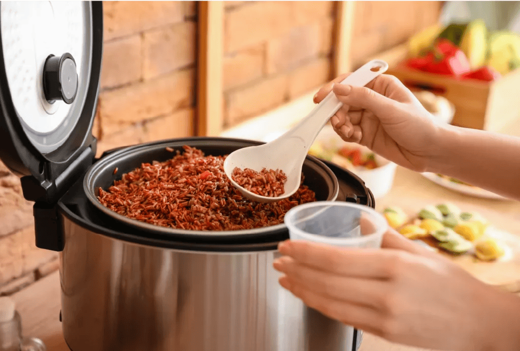 A chef spoons long-grain seasoned rice out of a rice cooker.