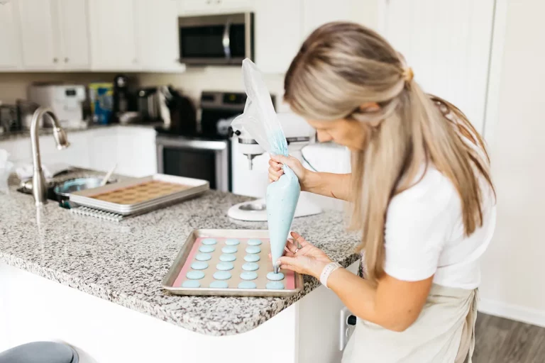 A woman with blonde hair prepares blue macarons for baking in her home kitchen.