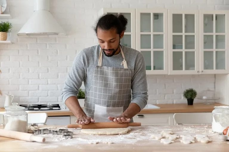 A young man rolls dough with a rolling pin in his home kitchen.