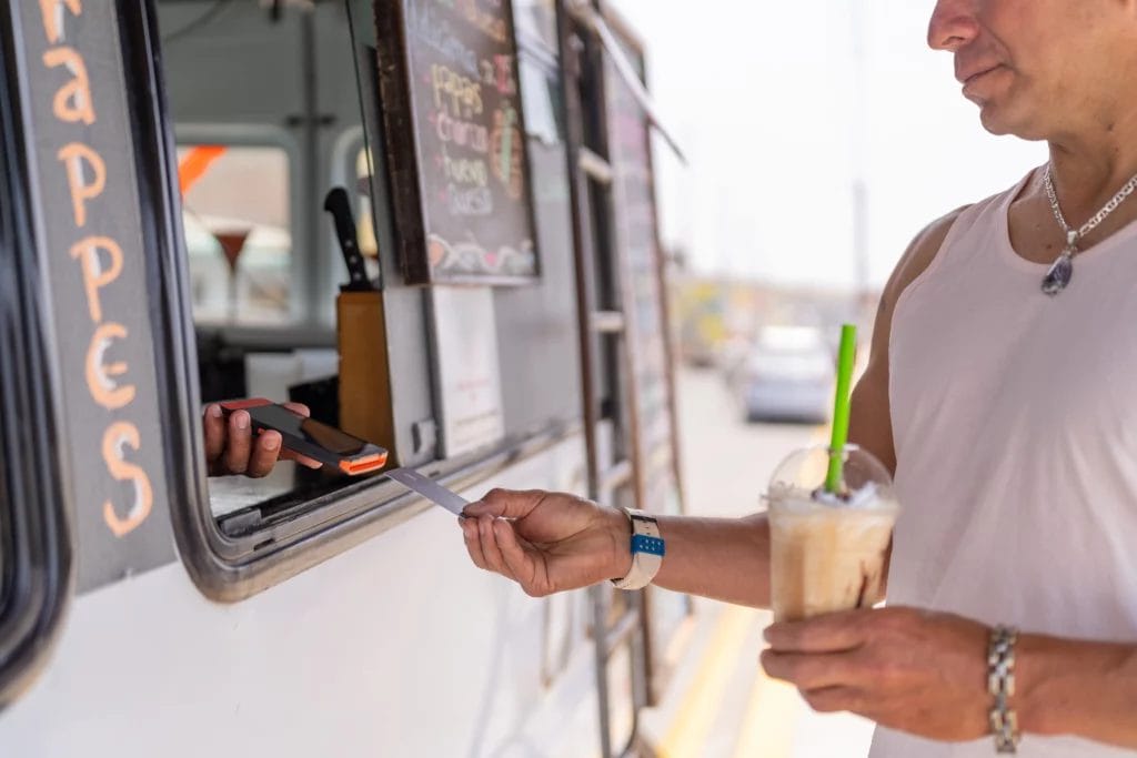 A man pays for his frappe at a coffee truck using a credit card.