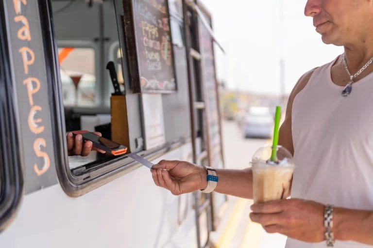 A man pays for his frappe at a coffee truck using a credit card.