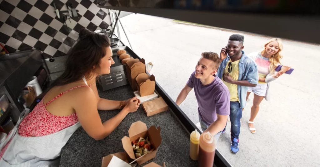 A bird's-eye view of a food truck employee taking a customer's order while two other customers stand behind him in line.