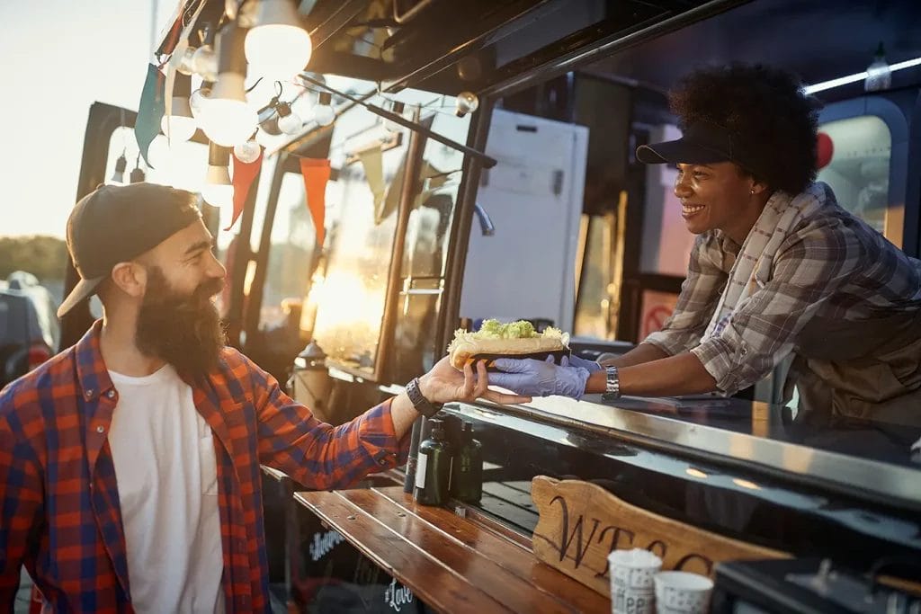 A man getting his order from the window of a food truck.