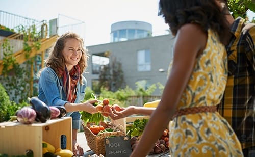 A vendor smiles at a customer while making a sale at a farmers market.
