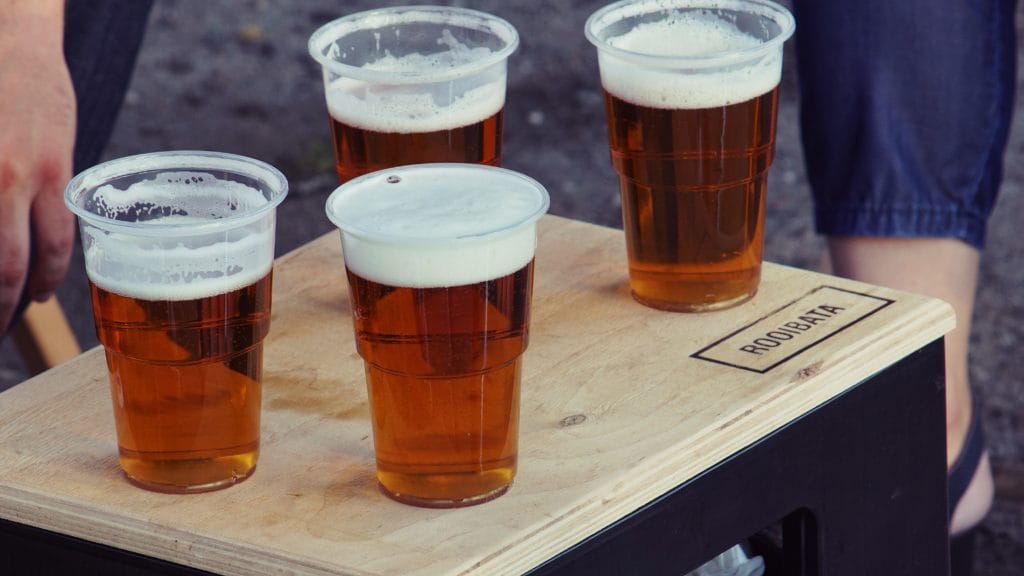 A wooden tray with four plastic cups of beer.