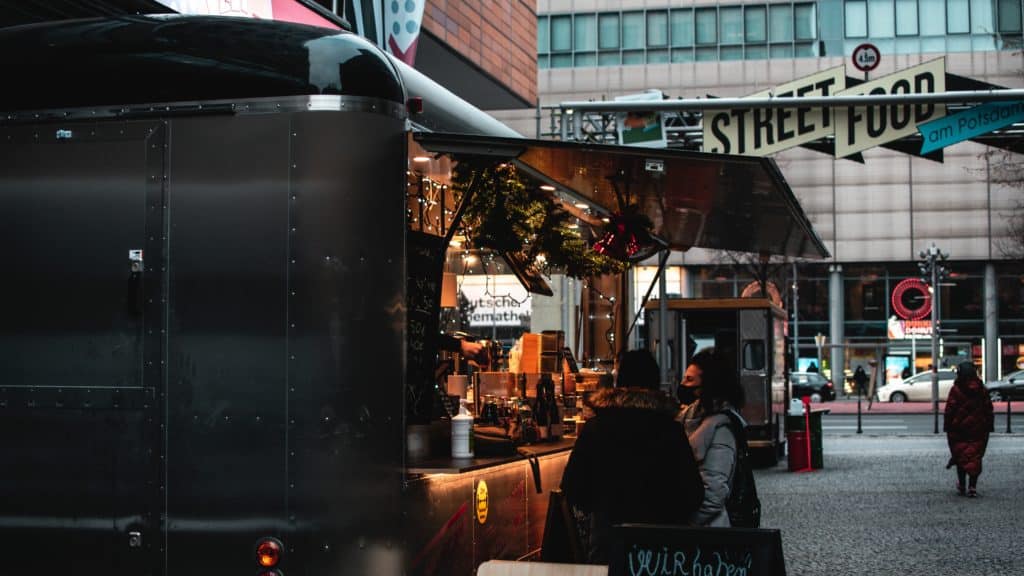 Two customers order from a black food truck on a downtown city street.