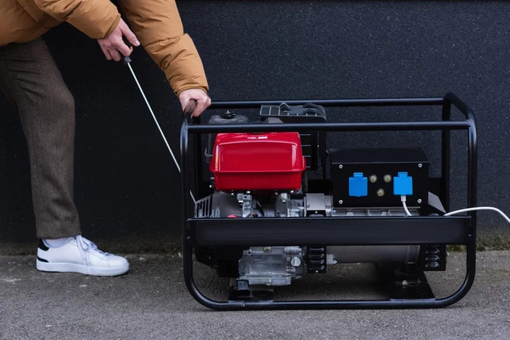 A person starting their portable generator outdoors on a paved surface.