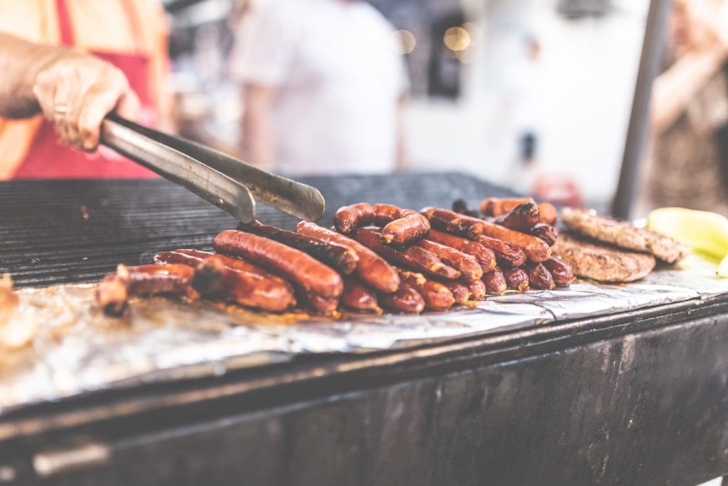 Person grilling hot dogs and burgers on large grill