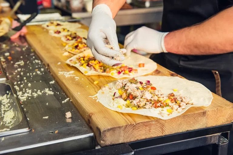 Close-up of a chef wearing gloves preparing burritos in a food truck.
