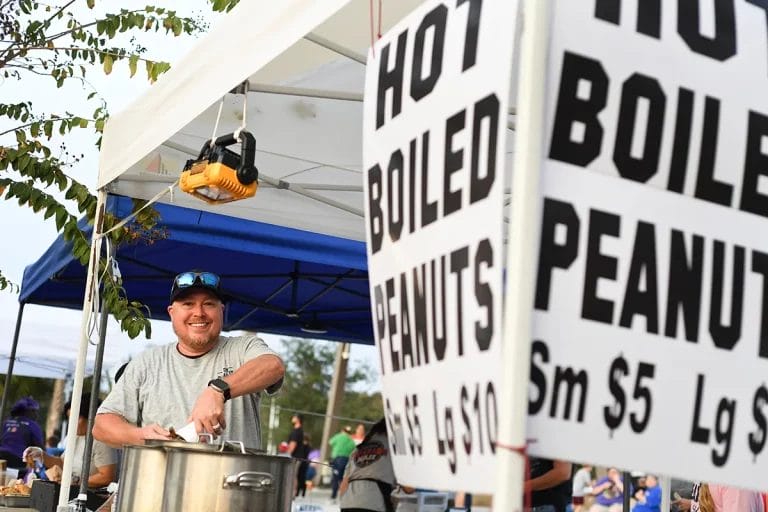 A vendor smiles at the camera behind his hot boiled peanuts stand at a food festival.