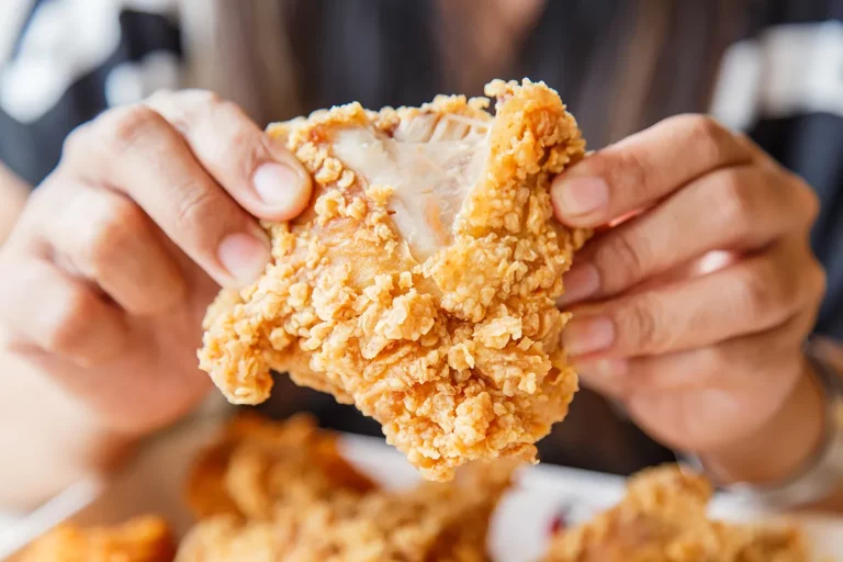 A closeup of hands holding fried chicken.