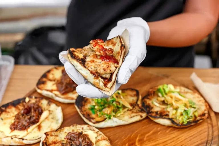 Person with gloved hands prepares seasoned tacos.