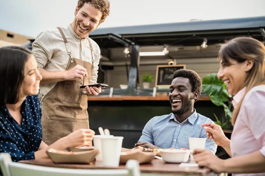 A food truck owner takes orders at a small table next to their truck.