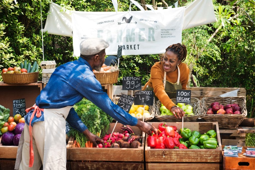 Two farmers market vendors arrange chalkboard signs around their produce stall.