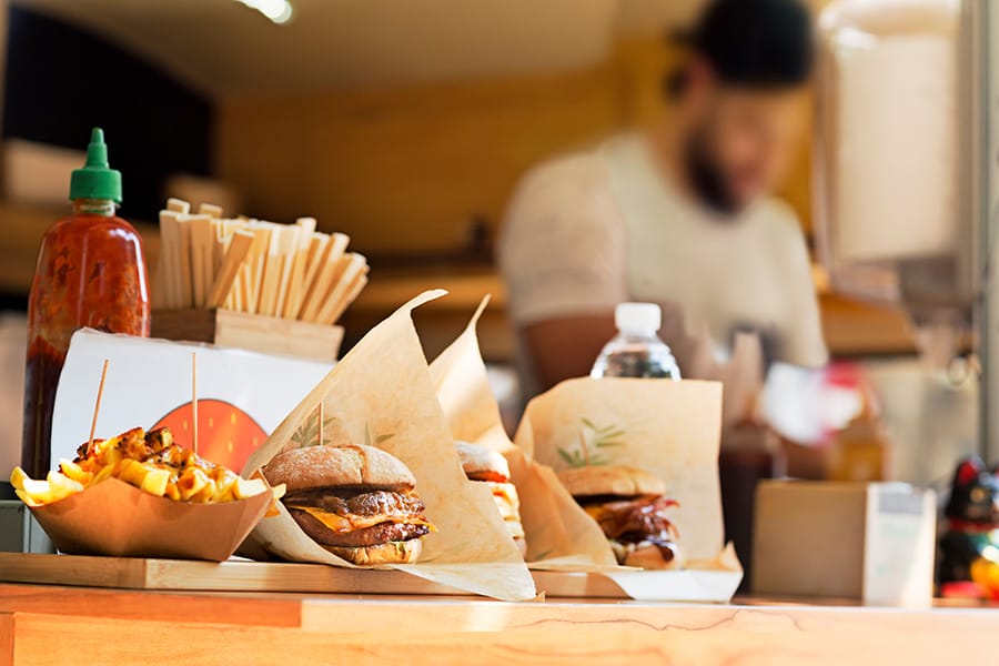 Sandwiches sitting on the counter of a food truck while an employee takes orders in the background.