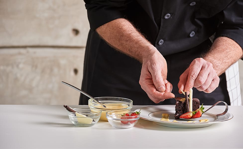 A private chef wearing an all-black uniform prepares chocolate cake for dessert.