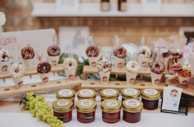 A display of food products from Fancy Nancy Boards including mini donuts on paper cones and jars of honey.