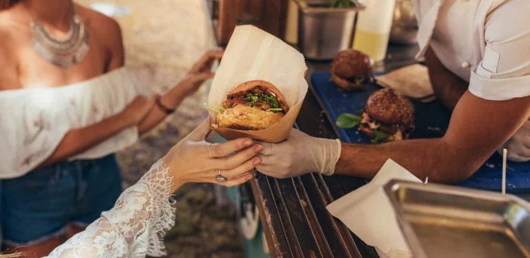 A food truck worker hands a hamburger to a customer out of a service window.