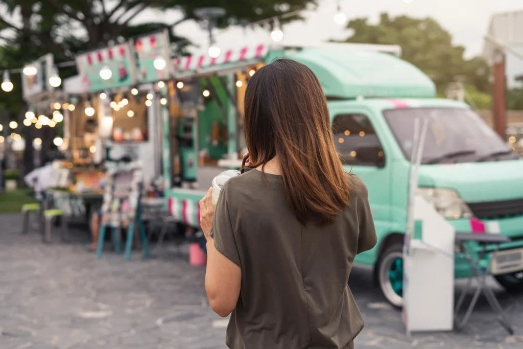 A woman with brown hair walking towards a turquoise food truck.