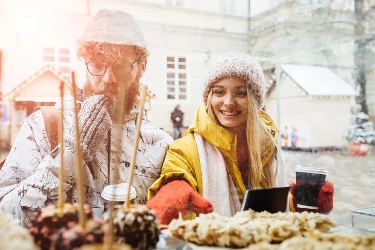 A man and a woman pick out candy apples at a snowy outdoor winter market.