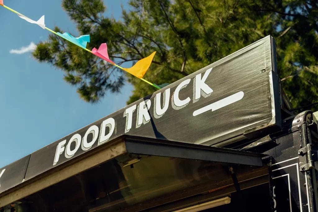 A signboard on a black food truck that reads "Food Truck" with colorful pennants hanging off it.