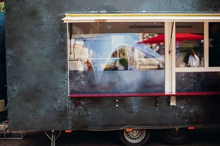 The ordering window on the side of a black food truck with to-go boxes visible through the glass.