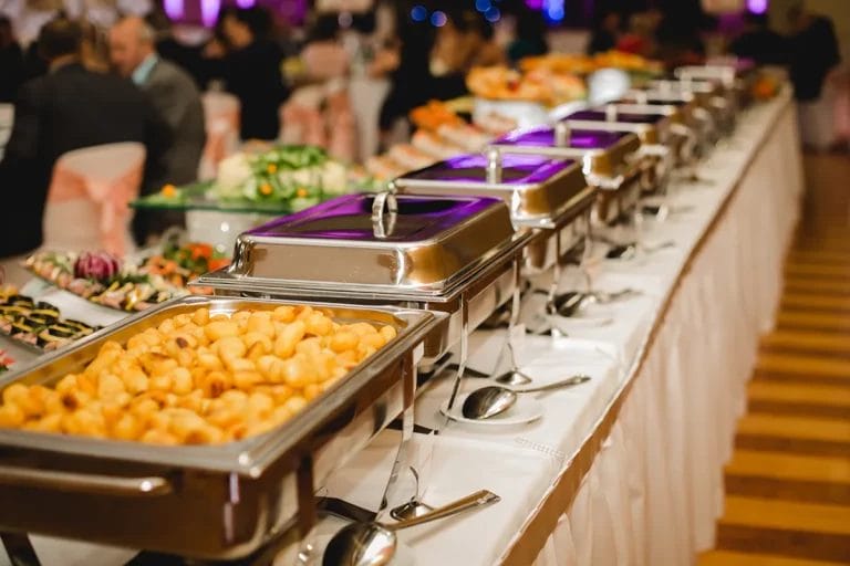 A row of heated serving dishes full of food on a buffet-style table at a catered event.