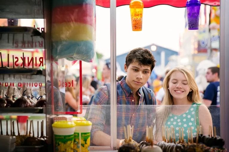 A young couple looks at a selection of candy apples on a concession stand.