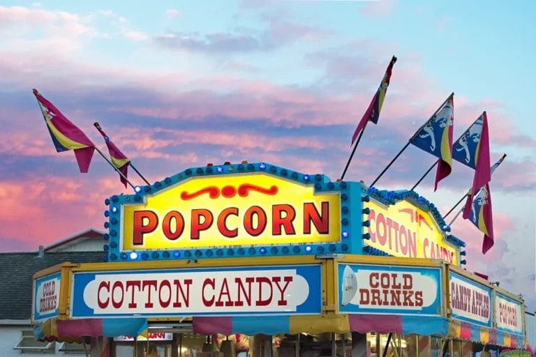 The top of a colorful popcorn concession stand at an outdoor fair during sunset.