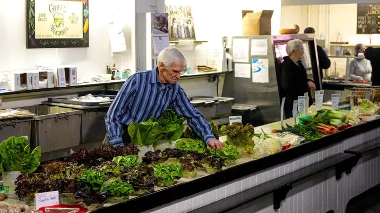 Earl Groff wears a blue striped shirt as he places a fresh head of lettuce out on his booth at Lancaster Central Market.