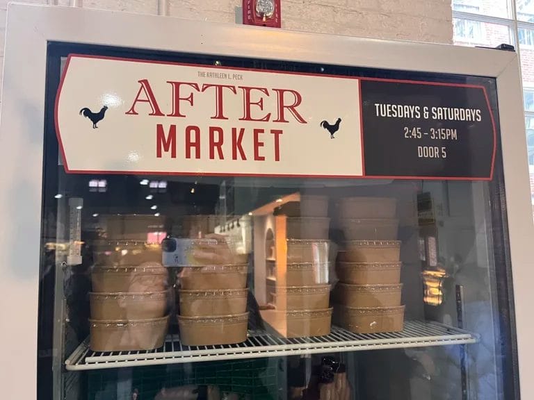 A fridge at Lancaster Central Market used for their After Market food donations program. The sign reads "The Kathleen L. Peck After Market. Tuesdays and Saturdays. 2:45 to 3:15 PM. Door 5."