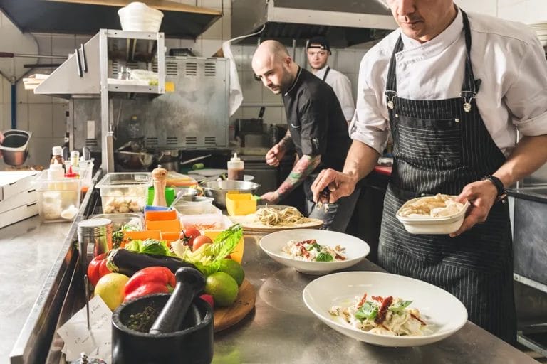 Several cooks prepare pasta dishes inside a commercial kitchen.
