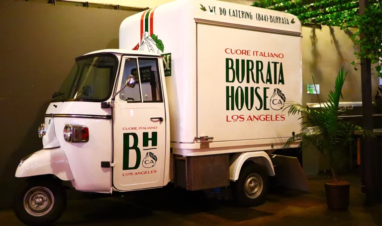A small white food truck parked indoors with branding that reads, "Cuore Italliano Burrate House Los Angeles CA."