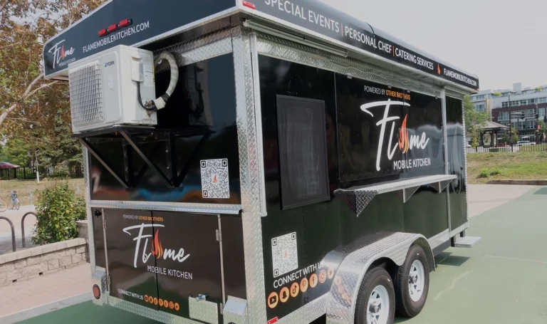 A small black food catering trailer parked outside and closed for business. The branding reads, "Flame mobile kitchen."