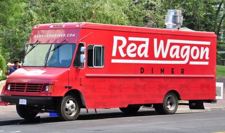 A red food truck parked outside on the curb to serve customers. The branding on the truck reads, "Red Wagon Diner."