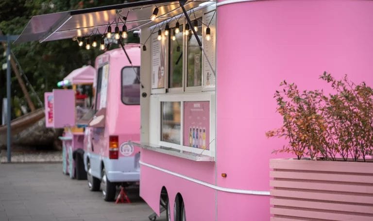 A row of three pink food trucks are open early on an empty street awaiting customers.