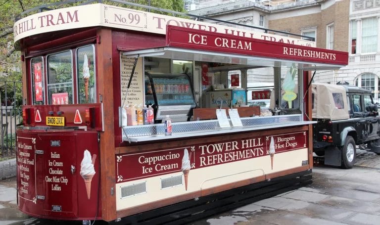 A red tram car converted into a food truck is ready to serve refreshments to patrons.