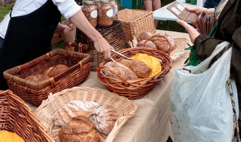 A close-up shot of a vendor using tongs to grab a loaf of fresh bread to package up for a customer.