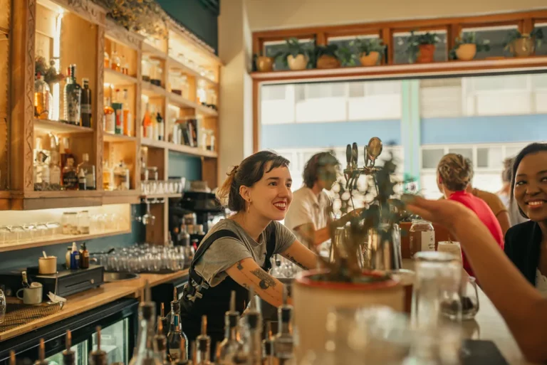 A bartender with tattoos smiles at customers behind a bar counter.