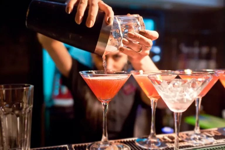 A close-up of a bartender preparing several cocktails along a bar.