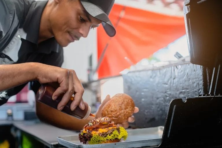 A chef in a food truck puts barbecue sauce on a burger.