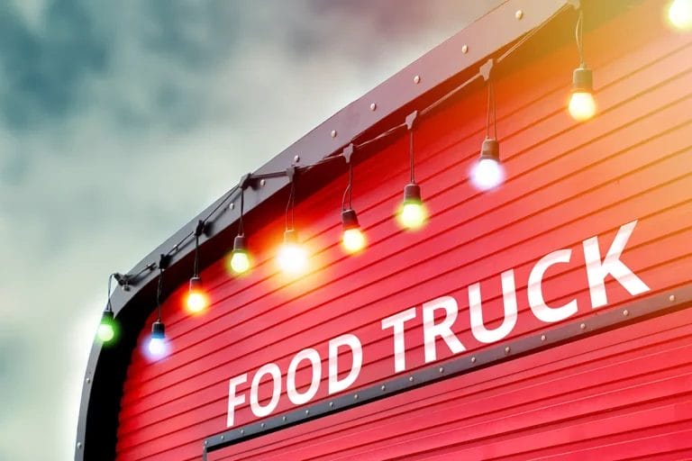The side of a red food truck decorated with colorful string lights that reads "Food Truck."