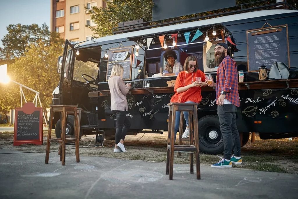 Several friends order from and hang out around a black food truck.