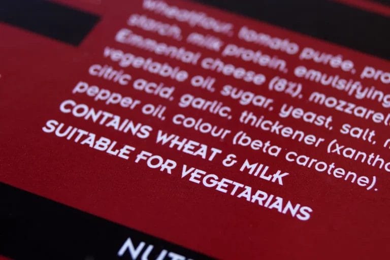 A close-up of a red and black ingredients list on a food package that says "Contains wheat and milk" and "Suitable for vegetarians."