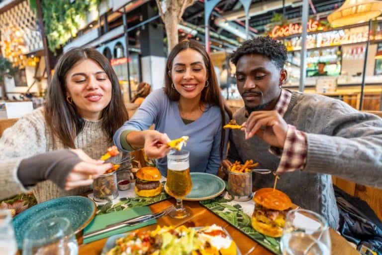 Three friends sharing nachos and eating burgers outdoors at a restaurant.