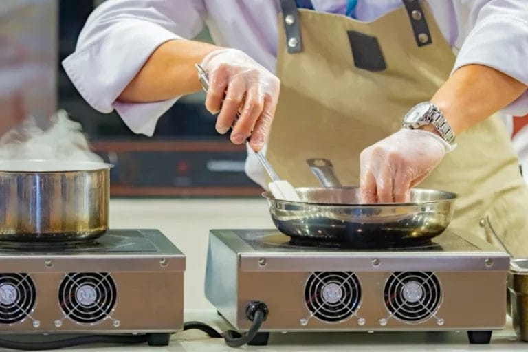 a catering chef preparing a meal with a frying pan over an induction cooktop